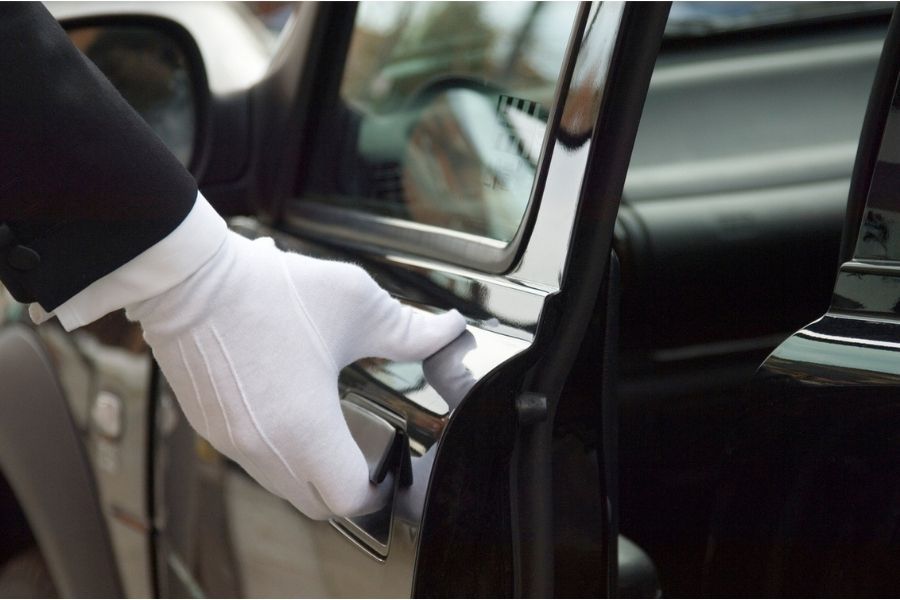 White-gloved chauffeur opening the door of a polished black luxury car.